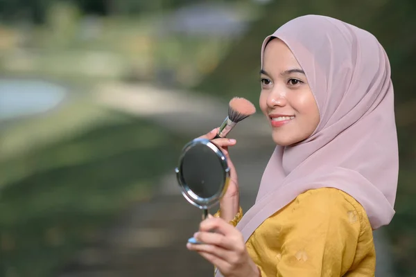 Asean woman applying makeup on her face, wearing traditional Malay  dress.