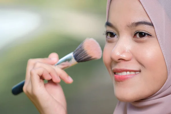 Asean woman applying makeup on her face, wearing traditional Malay  dress.