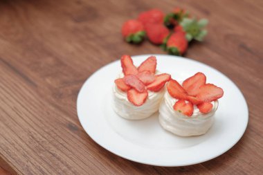 Krem şantili mini pavlovalar ve ahşap arka planda taze çilek.