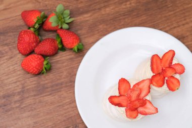 Krem şantili mini pavlovalar ve ahşap arka planda taze çilek.