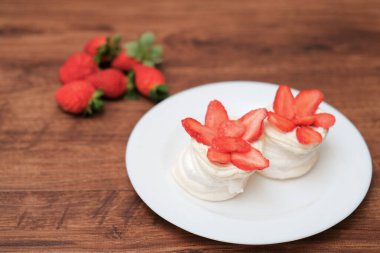 Krem şantili mini pavlovalar ve ahşap arka planda taze çilek.