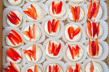 Krem şantili mini pavlovalar ve karton kutuda taze çilek.