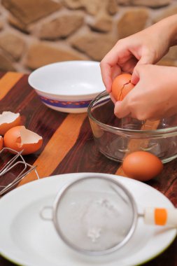 Kırık yumurtayı açık bir kasenin üzerinde tutan kadın eller. Pasta yapmak..