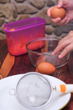 Kırık yumurtayı açık bir kasenin üzerinde tutan kadın eller. Pasta yapmak..