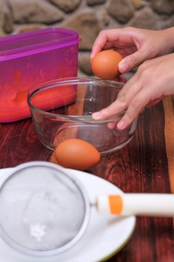 Kırık yumurtayı açık bir kasenin üzerinde tutan kadın eller. Pasta yapmak..