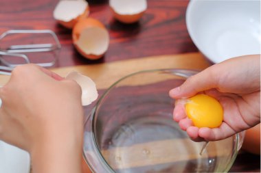 Kırık yumurtayı açık bir kasenin üzerinde tutan kadın eller. Pasta yapmak..