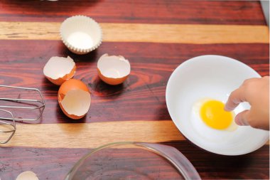 Kırık yumurtayı açık bir kasenin üzerinde tutan kadın eller. Pasta yapmak..