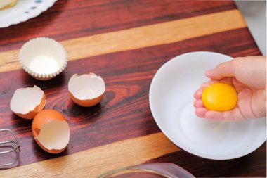 Kırık yumurtayı açık bir kasenin üzerinde tutan kadın eller. Pasta yapmak..