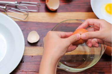 Kırık yumurtayı açık bir kasenin üzerinde tutan kadın eller. Pasta yapmak..