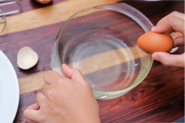 Kırık yumurtayı açık bir kasenin üzerinde tutan kadın eller. Pasta yapmak..