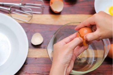 Kırık yumurtayı açık bir kasenin üzerinde tutan kadın eller. Pasta yapmak..