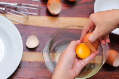 Kırık yumurtayı açık bir kasenin üzerinde tutan kadın eller. Pasta yapmak..