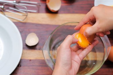 Kırık yumurtayı açık bir kasenin üzerinde tutan kadın eller. Pasta yapmak..