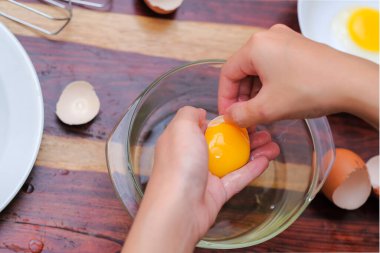 Kırık yumurtayı açık bir kasenin üzerinde tutan kadın eller. Pasta yapmak..