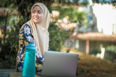 Başörtüsü takan İslami kız öğrencinin oturduğu ve gümüş dizüstü bilgisayar kullandığı fotoğraf