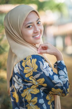 Bulanık arka planda krem rengi başörtüsü takan mutlu müslüman kadın portresi.