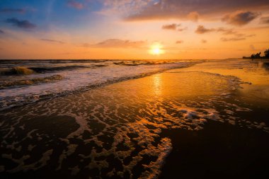 Güneşin doğuşu sırasında kumlu sahilde yumuşak mavi okyanus dalgalarıyla denizin üzerinde güzel bir bulut manzarası.