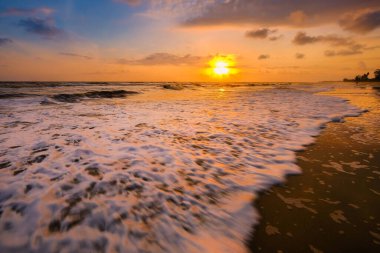 Güneşin doğuşu sırasında kumlu sahilde yumuşak mavi okyanus dalgalarıyla denizin üzerinde güzel bir bulut manzarası.