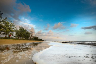 Güneşin doğuşu sırasında kumlu sahilde yumuşak mavi okyanus dalgalarıyla denizin üzerinde güzel bir bulut manzarası.