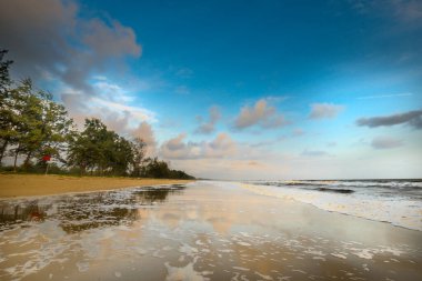 Güneşin doğuşu sırasında kumlu sahilde yumuşak mavi okyanus dalgalarıyla denizin üzerinde güzel bir bulut manzarası.