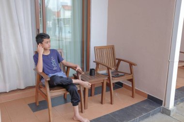 Young boy  sitting alone on a chair in backyard and using digital tablet