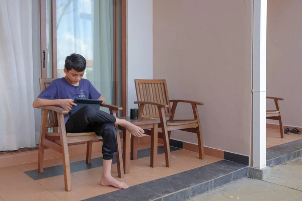 Young boy  sitting alone on a chair in backyard and using digital tablet