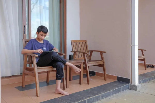 Young boy  sitting alone on a chair in backyard and using digital tablet