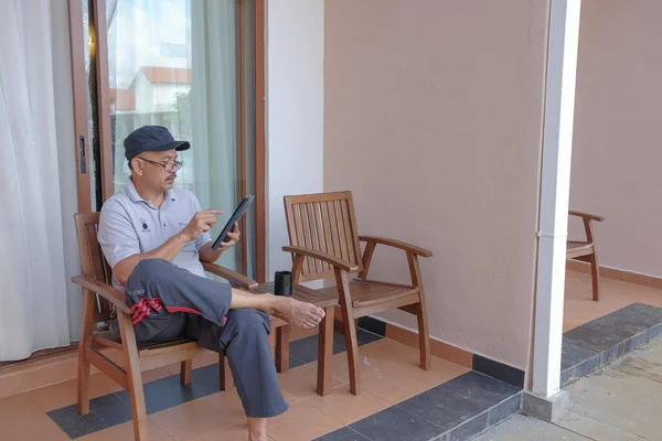 A man sitting alone on a chair in backyard and using digital tablet