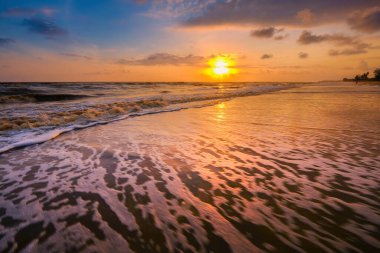 Güneşin doğuşu sırasında kumlu sahilde yumuşak mavi okyanus dalgalarıyla denizin üzerinde güzel bir bulut manzarası.