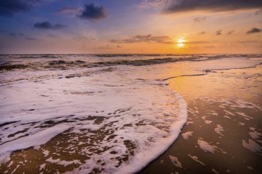 Güneşin doğuşu sırasında kumlu sahilde yumuşak mavi okyanus dalgalarıyla denizin üzerinde güzel bir bulut manzarası.