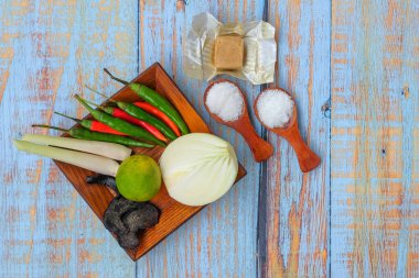 Tuzlu ahşap tabak, msg, zencefil, sarımsak, soğan, anahtar limon, biber, tavuk suyu küpü ve ahşap kesim tahtasının üzerinde limon otu..