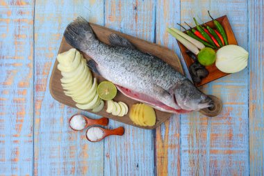 Ahşap kesim tahtasının üzerinde tuz, msg, zencefil, sarımsak, soğan, limon, biber ve limon otu ile Barramundi veya Asya deniz kabuğu balığı.