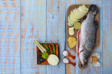 Ahşap kesim tahtasının üzerinde tuz, msg, zencefil, sarımsak, soğan, limon, biber ve limon otu ile Barramundi veya Asya deniz kabuğu balığı.