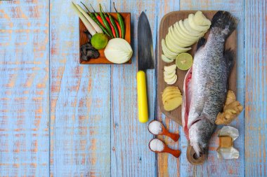 Ahşap kesim tahtasının üzerinde tuz, msg, zencefil, sarımsak, soğan, limon, biber ve limon otu ile Barramundi veya Asya deniz kabuğu balığı.