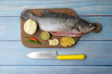 Bıçaklı, biberli, soğanlı, zencefilli, sarımsaklı ve ağaç kesme tahtasının üzerinde yeşil limonlu Barramundi veya Asya deniz kabuğu balığı..