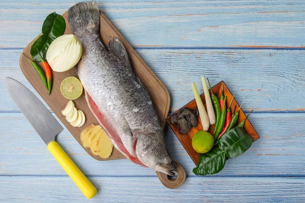 Bıçaklı, biberli, soğanlı, limonlu, kaffir limon yapraklı, zencefilli, sarımsaklı ve ağaç kesme tahtasının üzerinde yeşil limonlu Barramundi veya Asya deniz kabuğu balığı..