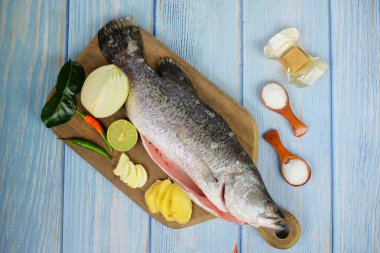 Ahşap zemin üzerinde baramundi, tuz, msg, zencefil, sarımsak, soğan, limon, biber ve limon otu olan tahta kesme tahtası..