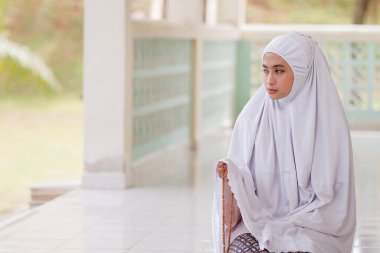 Elinde geleneksel İslami boncuklarla camide diz çökmüş dua eden bir kadın..