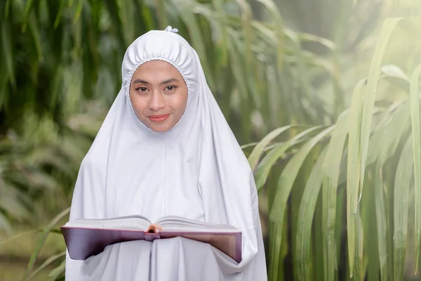 美しいイスラム教徒の女性が緑の木の庭でクルアーンを手に イスラム教育の概念 — ストック写真