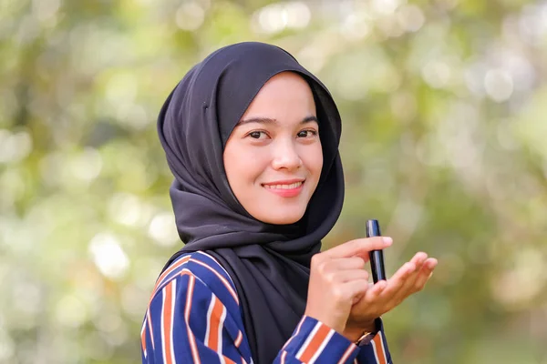 スマイリー美しいです若いですムスリム女性身に着けていますHijabと持っています口紅オンぼやけた背景 — ストック写真