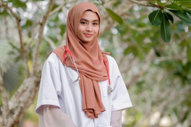 Hastane bahçesinde tesettürlü ve steteskoplu genç Asean kadın doktor. Tıbbi ve sağlık doktor hizmeti kavramı.