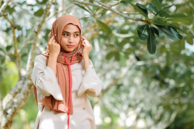 Ağaca yaslanırken stetoskop tutan gülümseyen kadın doktorların portresi.