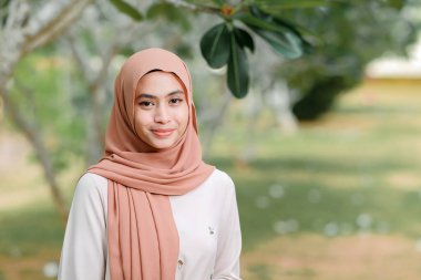 Güzel Müslüman kadın, bir ağacın altında gülümsüyor..