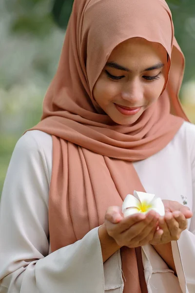 きれいなイスラム教徒の女性が木の下に立って白い花を保持 — ストック写真