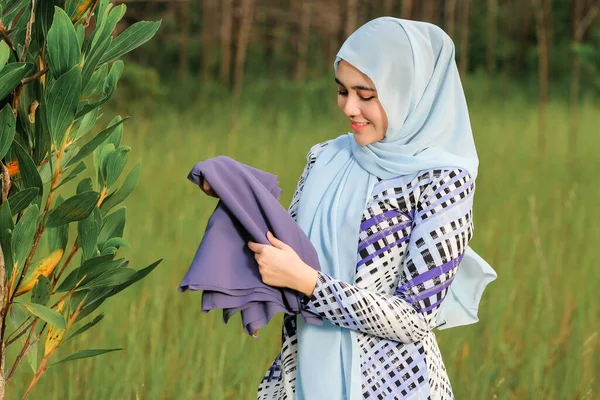 ファブリックを保持しながら緑の領域にポーズファッショナブルなヒジャーブスタイルで幸せな美しい若いモデルの肖像画 スタイリッシュなイスラム教徒の女性のヒジャーブファッションライフスタイルの肖像コンセプト — ストック写真