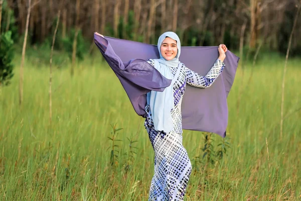 ファブリックを保持しながら緑の領域にポーズファッショナブルなヒジャーブスタイルで幸せな美しい若いモデルの肖像画 スタイリッシュなイスラム教徒の女性のヒジャーブファッションライフスタイルの肖像コンセプト — ストック写真