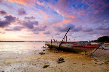 Güzel bir gökyüzüyle gün batımında sahilde mahsur kalmış eski bir ahşap balıkçı teknesi.