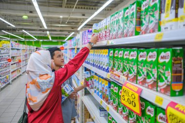 Muadzam Şah, Malezya - 8 Mart 2020: Süpermarkette alışveriş yapan, ürün bilgisi okuyan, süt tutan, fiyatları ve kaliteyi karşılaştıran, günlük giysiler giyen gençler çekici görünümlü.