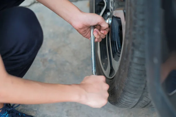 A teenager is changing a wheel on a car. Car on maintenance, repair service.