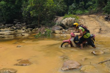 Rompin, Malezya - 11 Ekim 2020: Bir motosikletli bir motosikleti nehirden geçirir. Seyahat ve arkadaşlık kavramı